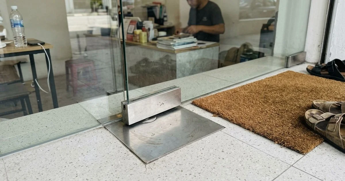 Floor spring set into a tiled floor beneath a glass door pivot